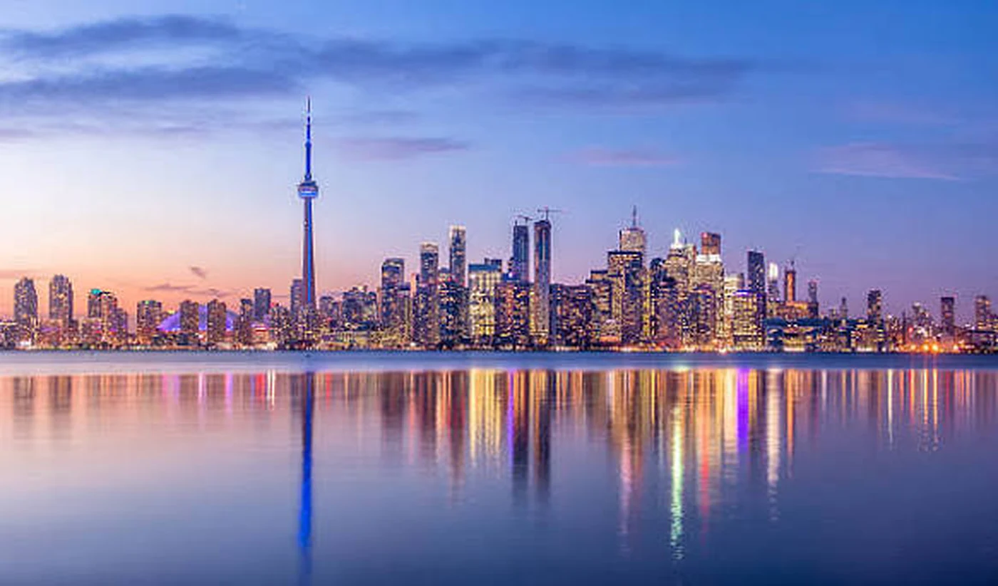 Toronto skyline at dusk with CN Tower and city lights reflected on Lake Ontario
