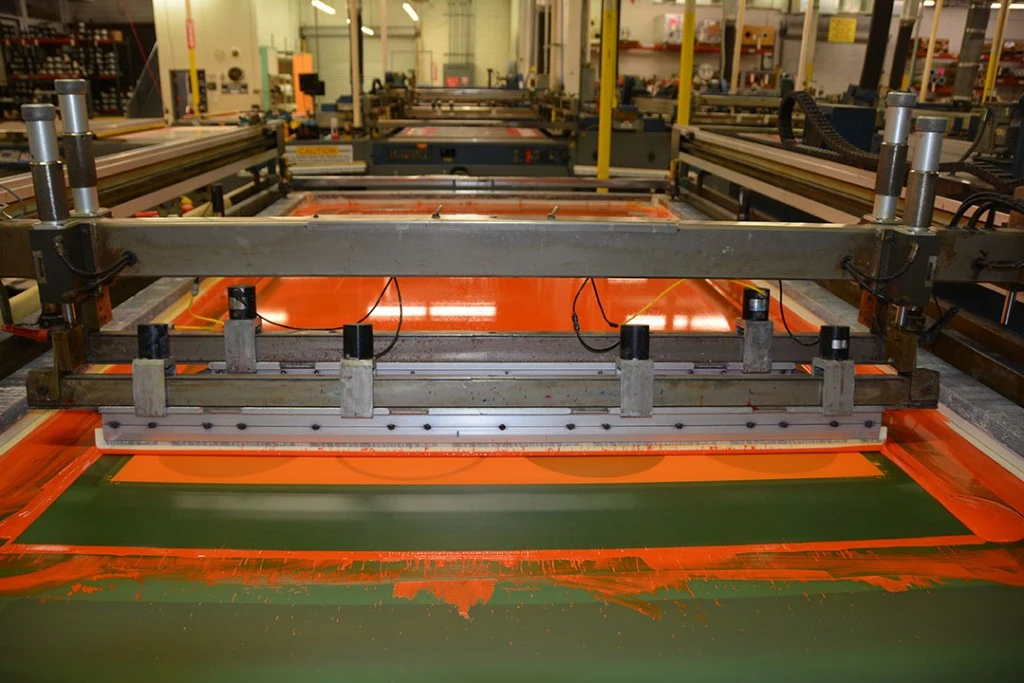 Silkscreen squeegee spreading ink across a large-format print on the production floor
