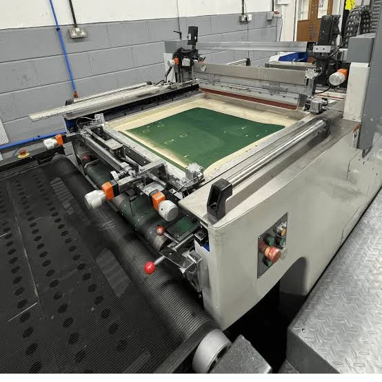 Automatic silkscreen printing press with screen frame and conveyor belt in a production shop